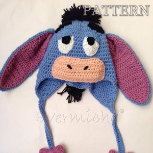 Puede incluir: Un gorro de punto azul con orejas rosas y una cara de burro. El gorro tiene borlas negras y lazos rosas en los extremos de las borlas. El gorro está etiquetado con "PATTERN" y "evernicha".