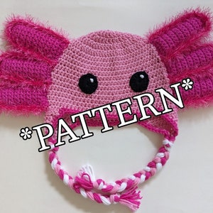 May include: A handmade crochet axolotl hat in shades of pink, featuring large, fringed gills and black eyes. The hat has a braided chin strap with pink and white yarn. The word "PATTERN" is printed across the image.