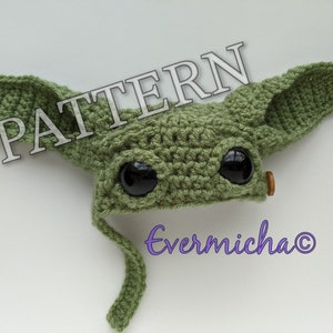 May include: Green crocheted hat with large ears and black eyes. The hat has a long tail that hangs down. The text "PATTERN" is written in white on a black background in the top left corner of the image. The text "Evermicha©" is written in purple in the bottom right corner of the image.