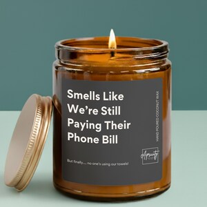 Candle labeled “Smells Like We're Still Paying Their Phone Bill – But finally… no one’s using our towels!” displayed on a neutral background. The design is clean and playful, making it a funny and relatable gift for empty nesters.