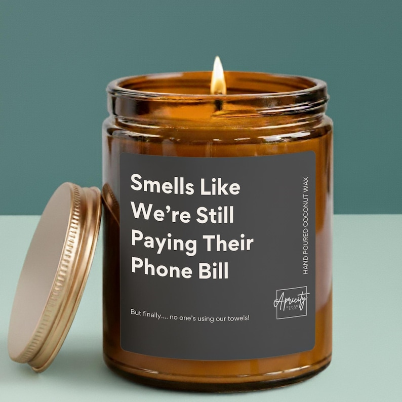 Candle labeled “Smells Like We're Still Paying Their Phone Bill – But finally… no one’s using our towels!” displayed on a neutral background. The design is clean and playful, making it a funny and relatable gift for empty nesters.