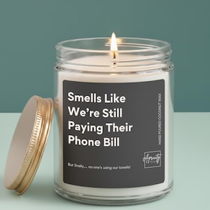 Candle labeled “Smells Like We're Still Paying Their Phone Bill – But finally… no one’s using our towels!” displayed on a neutral background. The design is clean and playful, making it a funny and relatable gift for empty nesters.