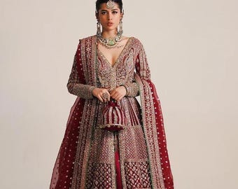May include: A burgundy formal gown with intricate gold and silver embroidery. The dress features a deep V-neck, long sleeves, and a flowing skirt. A matching purse and sheer shawl complete the ensemble. The gown is adorned with sparkling embellishments.