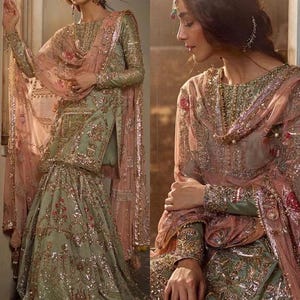 May include: An elegant, sage green and pink embroidered formal dress. The dress features intricate gold embellishments, a matching dupatta, and a flowing skirt. The sleeves and neckline are also adorned with detailed embroidery, creating a luxurious look.