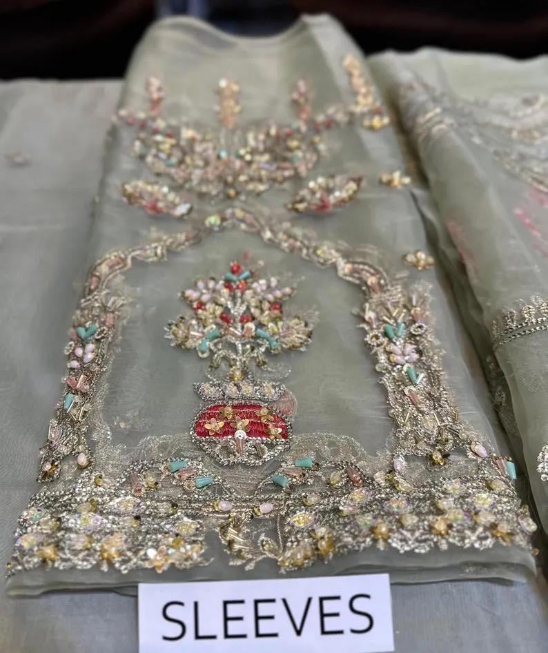 May include: A light green, sheer fabric with intricate embroidery. The embroidery features floral and geometric patterns in shades of gold, red, pink, and blue. The word "SLEEVES" is printed on a white label at the bottom.