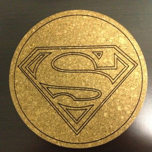 May include: A round cork coaster with a black Superman logo in the center.