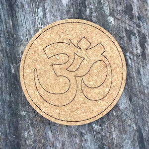 May include: A cork coaster with a brown background and a black outline of the Om symbol.