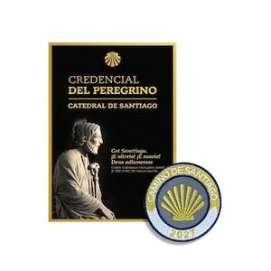May include: A black rectangular Credencial del Peregrino document from the Catedral de Santiago featuring a gold scallop shell icon, a statue of a bearded figure, and text, alongside a circular embroidered patch with a gold shell and 2021.