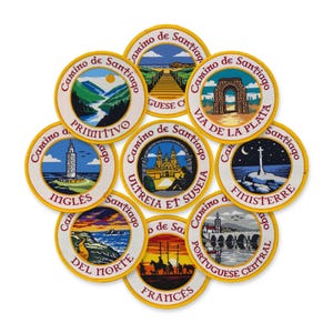 May include: A collection of embroidered patches with the words "Camino de Santiago" and various route names. Each patch features a different scenic illustration, including landscapes, architecture, and historical landmarks, with a yellow border.