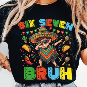 Może przedstawiać: Czarny t-shirt z kolorową grafiką przedstawiającą chłopca z kreskówki w sombrero i okularach przeciwsłonecznych wykonującego ruch dab. Koszulka zawiera słowa "SIX SEVEN BRUH" w żywych kolorach, wraz z obrazami tacos, marakasów i papryczki chili.