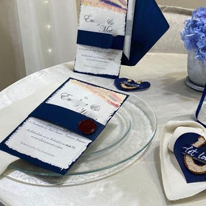 May include: Navy blue wedding invitations with watercolour accents and a wax seal. The invitations are displayed with a matching envelope and decorative elements, including a heart-shaped tag that says "Let love".