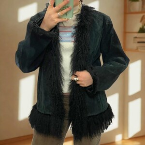 May include: A dark green suede jacket with black faux fur trim on the collar, front, and cuffs. The jacket has a classic shape and a soft, textured look. This outerwear item is suitable for various occasions.