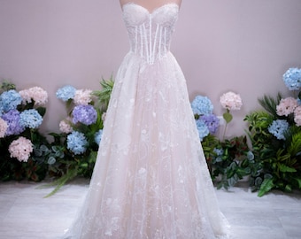 May include: A strapless floor-length gown featuring a structured corset-style bodice with vertical boning and a sweetheart neckline. The skirt is made of layered tulle with white floral embroidery and subtle sequin embellishments throughout the fabric.