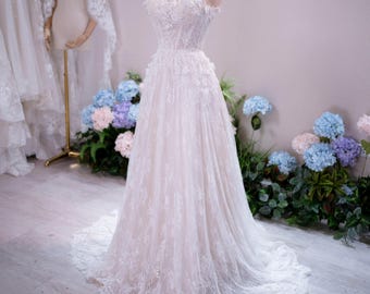 May include: A strapless floor-length wedding dress featuring a sweetheart neckline, a fitted bodice with intricate white lace floral appliqués, and a full tulle skirt that extends into a train, displayed on a mannequin wearing a gold crown.
