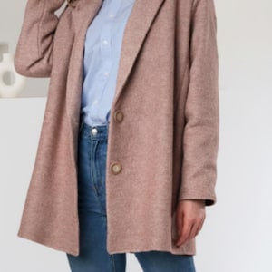 Puede incluir: Un blazer rosa empolvado con dos botones marrones. El blazer se lleva sobre una camisa abotonada azul claro y vaqueros azules. El blazer tiene solapas clásicas y un corte relajado.