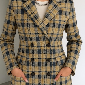 Puede incluir: Una blazer cruzada con un estampado a cuadros en beige y azul marino. La blazer tiene solapas con muescas, dos filas de botones oscuros y dos bolsillos delanteros. La persona lleva una camisa blanca debajo.