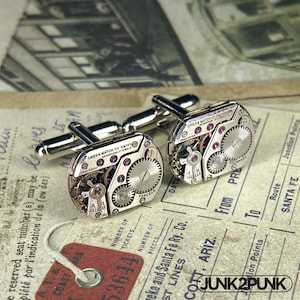May include: A pair of silver-toned cufflinks crafted from vintage Omega watch movements. Each piece features exposed gears, metallic plates, and small red jewels. The text OMEGA WATCH CO SWISS SEVENTEEN 17 JEWELS is engraved on the top surface of each.