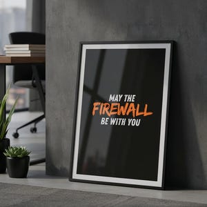 Può includere: Un poster nero incorniciato con bordo bianco, appoggiato a un muro grigio. Il poster recita "MAY THE FIREWALL BE WITH YOU" in testo arancione e bianco. Sullo sfondo un tavolo, un laptop e delle piante.