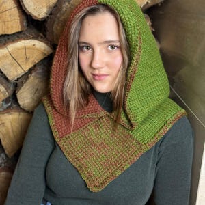 May include: A handmade, two-toned hood in shades of green and brown. The hood is knitted with a textured stitch and features a square neckline. The hood is designed to be worn over the head and shoulders, providing warmth and style.