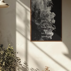 May include: A framed art print with a dark brown wooden frame. The artwork features a black background with a wispy, white smoke-like design. The text "Break The Cycle. Raise The Bar. Set A New Standard." is printed on the artwork.