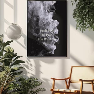 May include: Black framed art print with white text that reads "Push Past The Point You Want To Quit." The artwork features a black background with a white, smoky design. The print is displayed on a white wall.