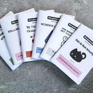 May include: A collection of small white zines with titles such as "Cats do Rule Actually" and "Amphibians of N". Each zine features black and white designs and text, with coloured accents. The zines are displayed on a grey surface.