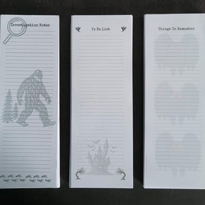 Pode incluir: Três blocos de notas brancos com ilustrações e texto cinza. Um diz "Investigation Notes" com uma lupa e Bigfoot. Outro diz "To Do List" com uma casa assombrada. O último diz "Things To Remember" com fantasmas.