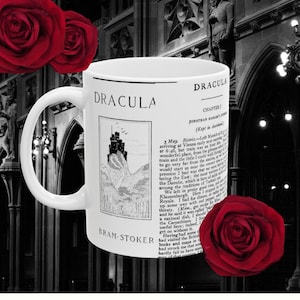 May include: A white ceramic mug featuring the title "DRACULA" and an illustration of a castle on a cliff, with text from the novel. The mug is decorated with red roses and the author's name, Bram Stoker.