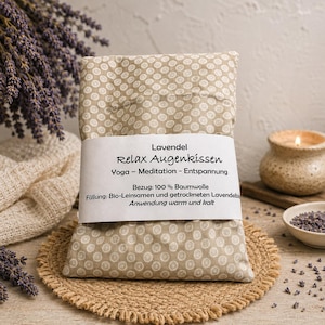 Könnte beinhalten: Ein rechteckiges Augenkissen aus beigem Stoff mit weißem Kreis-Muster. Eine weiße Papierbanderole ist um die Mitte gewickelt mit dem Text: Lavendel Relax Augenkissen Yoga - Meditation - Entspannung Bezug: 100 % Baumwolle Füllung: Bio-Leinsamen und getrockneten Lavendelblüten Anwendung warm und kalt.