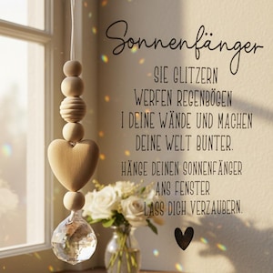 Könnte beinhalten: Ein Holz-Sonnenfänger mit Herz- und Kristallanhänger hängt in der Nähe eines Fensters. Der Sonnenfänger ist an einer Schnur aufgehängt und hat eine Reihe von Holzperlen. Der Text auf Deutsch lautet "Sonnenfänger" und andere Sätze.