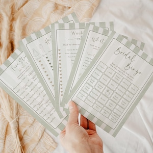 May include: A collection of bridal shower game cards with a green and white striped border. The cards include games like "Bridal Bingo" and "Love Story Mad Libs". The text is in a delicate, handwritten style.