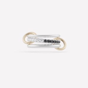 May include: A multi-layered ring with a modern design. The ring features three bands: two silver-colored bands and one band with alternating white and black gemstones. The ring is connected by two gold-colored loops.