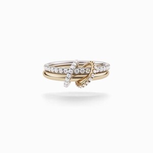May include: Three stacked rings, one gold, one silver, and one gold and silver. The silver ring is encrusted with small, clear stones. Two additional rings, also encrusted with stones, are positioned across the stacked rings.