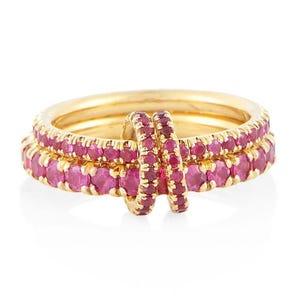 Könnte beinhalten: Ein Set aus drei goldenen Ringen. Zwei sind gestapelt, jeder mit einem Band aus rosa Edelsteinen. Ein kleinerer Ring verbindet die beiden größeren. Die Ringe sind vor einem weißen Hintergrund.