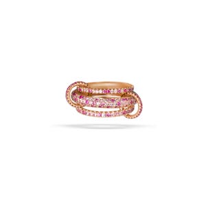 Könnte beinhalten: Ein roségoldener Ring mit drei ineinandergreifenden Bändern. Jedes Band ist mit rosa und weißen Edelsteinen besetzt. Der Ring ist vor einem weißen Hintergrund platziert, der das komplizierte Design und die Farbe des Schmucks hervorhebt.