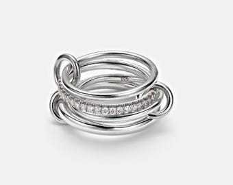 May include: A silver ring with multiple interlocking bands. One band is encrusted with small, clear stones. The ring is made of polished metal and has a modern design. The ring is marked with "925".