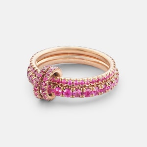 Può includere: Anelli in oro rosa con pietre preziose rosa. Gli anelli sono impilati, con un anello che forma un nodo. Le pietre preziose rosa sono posizionate vicine, creando una fascia continua di colore. Gli anelli sono su sfondo bianco.