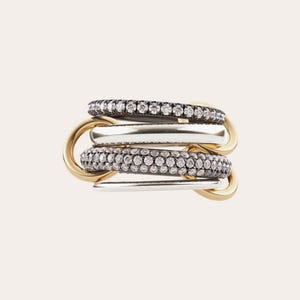 May include: A stack of rings in gold, silver, and black. The rings feature a combination of smooth metal bands and bands encrusted with small, sparkling stones. The rings are interlocked, creating a layered effect.