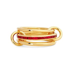 Op de afbeelding: Een gouden ring met een meerlaags ontwerp bestaande uit drie met elkaar verbonden banden. De middelste band is ingelegd met een doorlopende rij rechthoekige, levendig rode robijnen in een kanaalzetting, terwijl de buitenste banden glad zijn.