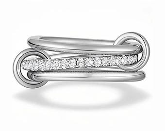 May include: A silver ring with three interlocking bands. One band is encrusted with small, clear gemstones. The ring has a polished finish and is designed with a modern, minimalist aesthetic. The ring is a piece of jewelry.
