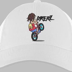 May include: White baseball cap with a mesh back and a cartoon graphic of a person riding a bicycle in a wheelie. The graphic includes the word "BIKERZ" in black lettering. The person in the graphic is wearing a red shirt, blue shorts, and a yellow backpack.