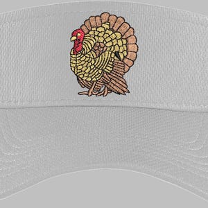 May include: A light gray visor featuring an embroidered turkey design. The turkey has a red head, yellow and brown body, and a fanned-out tail. The visor is made of a breathable fabric, ideal for outdoor activities.