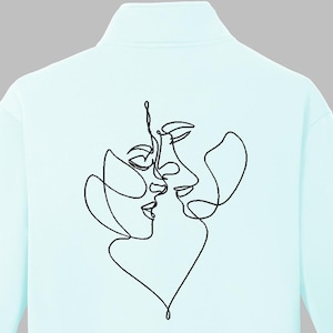 以下が含まれることがあります： 2つの顔がキスをしている黒い線画のデザインが施された、水色のスウェットシャツ。下部にはハートの形が描かれています。スウェットシャツはハイカラーです。