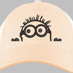 May include: A beige baseball cap with a mesh back and a curved brim. The cap features an embroidered cartoon character with large black eyes and spiky hair. The character is peeking over the brim.