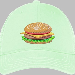 May include: A light green baseball cap featuring an embroidered image of a hamburger. The burger has a sesame seed bun, a red tomato slice, yellow cheese, a brown patty, and green lettuce. The cap has a curved brim and a mesh back.