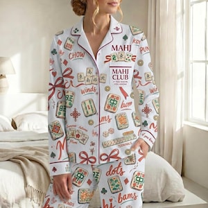 May include: White pajama set with a Mahjong theme. The set features a button-down shirt and pants, adorned with Mahjong tiles, Chinese characters, and the text "MAHJ CLUB". The design includes red accents and ribbon details.