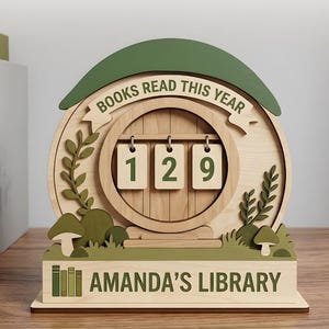 Puede incluir: Contador de libros de madera con el texto "BOOKS READ THIS YEAR" y los números "129". La base dice "AMANDA'S LIBRARY". El diseño incluye detalles en verde y una estética de cuento de hadas.