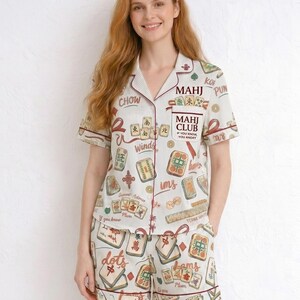 May include: Cream-colored pajama set with a Mahjong tile print and red trim. The short-sleeved top and shorts feature a striped pattern and various Mahjong tile illustrations. The top has the text "MAHJ CLUB" and other Chinese characters.