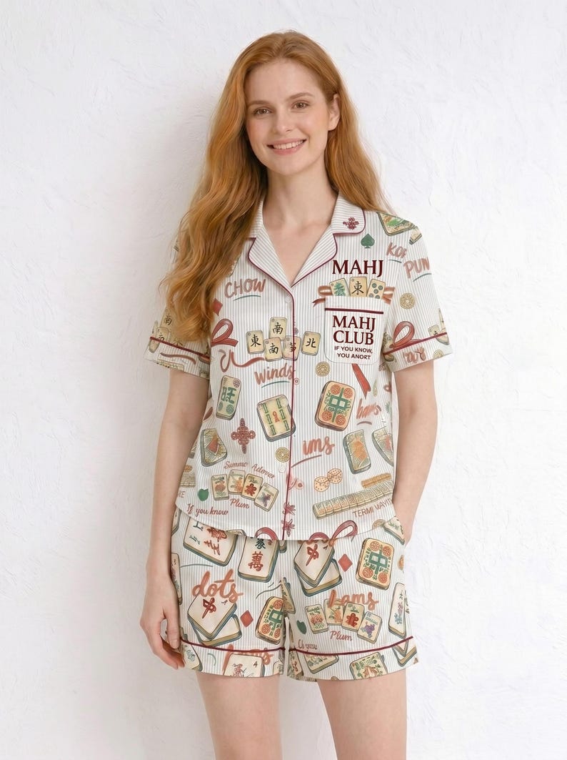 May include: Cream-colored pajama set with a Mahjong tile print and red trim. The short-sleeved top and shorts feature a striped pattern and various Mahjong tile illustrations. The top has the text "MAHJ CLUB" and other Chinese characters.