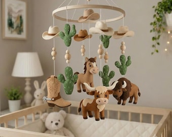May include: A nursery mobile featuring felt figures of a brown horse, a longhorn cow, a bison, green cacti, and tan cowboy hats suspended from a circular wooden frame with white strings and wooden beads, creating a western-themed hanging decor.